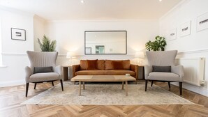 A living room with a sofa set, two armchairs, a coffee table, and a large mirror on the wall. - 2 South Beach Court - Beach Apartment (Tenby)