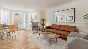 A modern living room with a brown leather sofa, a wooden coffee table, and a striped armchair. There is a dining area with a glass table and chairs, and a large mirror on the wall. - 2 South Beach Court - Beach Apartment (Tenby)