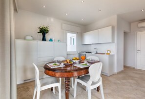 Une cuisine moderne avec des meubles blancs, une table à manger avec des chaises et un petit îlot central doté d’un évier.