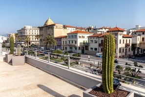 Une terrasse sur le toit offrant une vue sur le paysage urbain, avec des bâtiments aux toits recouverts de tuiles rouges et des palmiers.