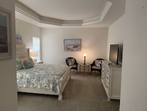 Un dormitorio con una cama, dos sillas, una mesita, un aparador y un cuadro en la pared.