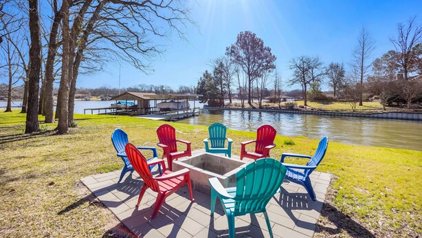 Une terrasse au bord du lac, avec des fauteuils Adirondack et un foyer, entourée d’arbres et d’un quai.