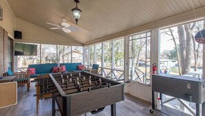 Une pièce avec une table de baby-foot, un canapé avec des coussins, une télévision et de grandes fenêtres donnant sur un lac.
