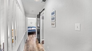 Un couloir avec un lit en arrière-plan, un mur blanc orné d’une enseigne et un luminaire.
