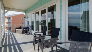 Ett takförsett utomhusområde med sittplatser, inklusive stolar och en soffa, och utsikt över havet genom stora fönster.