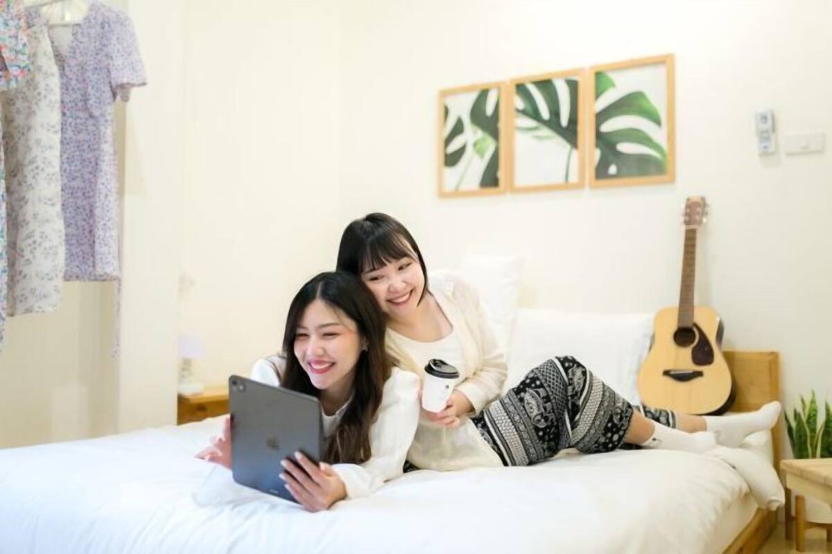 Two people lying on a bed with a guitar and a plant in the background.