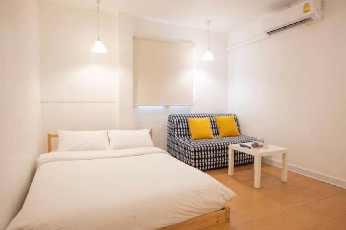 A bedroom with a bed, a sofa, a small table, and an air conditioning unit.
