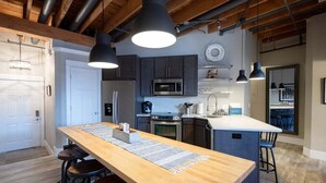 A modern kitchen with wooden countertops, dark cabinets, and stainless steel appliances. There is a long island with stools and pendant lighting. - Beautifully decorated in Historical Piano Factory (Grand Haven)
