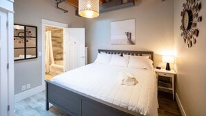 A bedroom with a bed, bedside table, lamp, and a wall clock. - Beautifully decorated in Historical Piano Factory (Grand Haven)