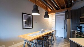A modern kitchen with a wooden table, bar stools, and a stainless steel refrigerator. - Beautifully decorated in Historical Piano Factory (Grand Haven)