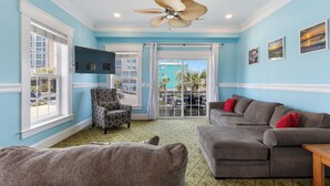 A room with a blue wall, a ceiling fan, a gray sofa with red cushions, a patterned armchair, and a television on the wall. - Ocean view, Walkable to Everything in the heart of Carolina Beach (Carolina Beach)
