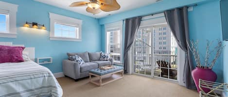 Ein Schlafzimmer mit einem Bett, einem grauen Sofa, einer hölzernen Bank, einem großen Fenster und einem Balkon.