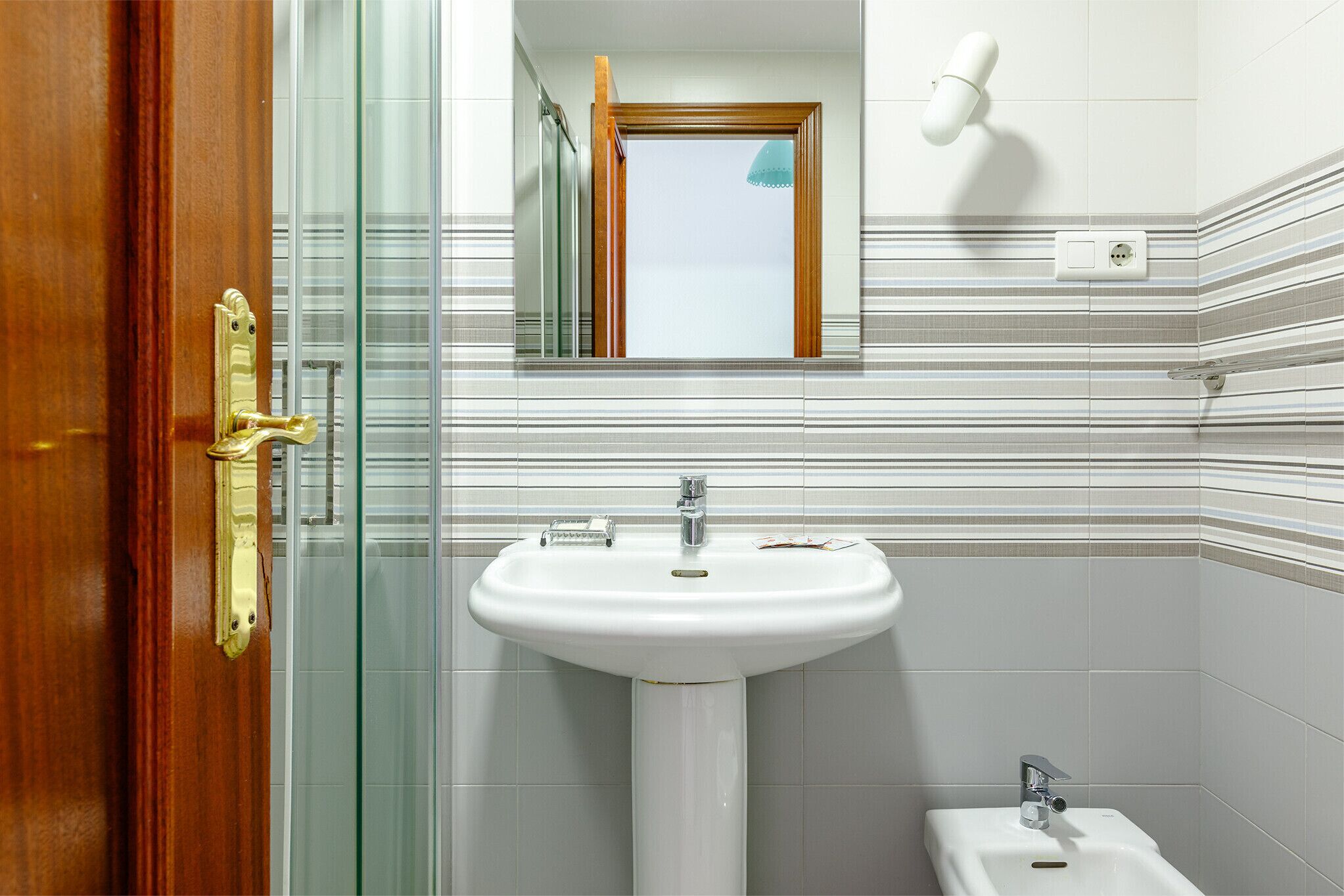 Une salle de bain avec un lavabo blanc, un miroir et une douche.