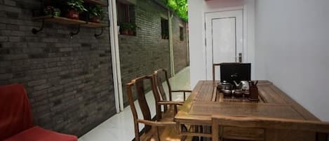 A dining area with a wooden table and chairs, a red chair, a white door, and a brick wall with shelves.