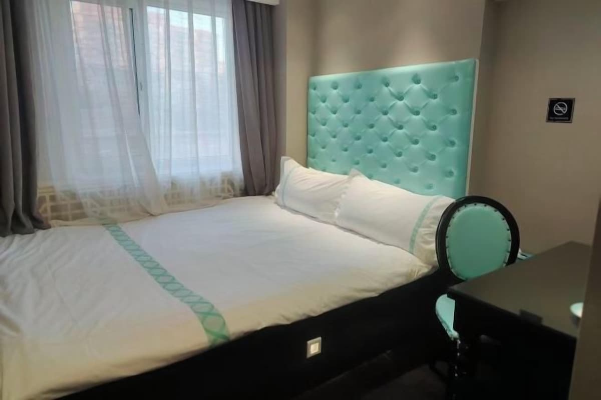 Una habitación de hotel con una cama, una mesita de noche, un espejo y una ventana con cortinas.