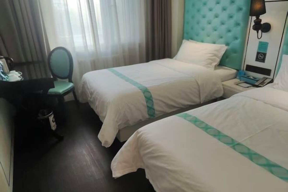 Hotellihuone, jossa on kaksi sänkyä, työpöytä, tuoli ja ikkuna, jossa on verhot.
