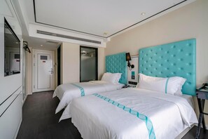 Habitación de hotel con dos camas, un ventanal grande, un minibar y la puerta del baño.