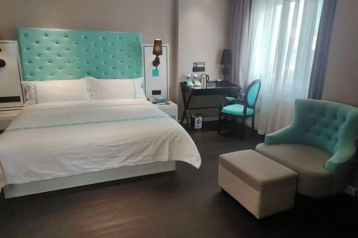 Hotellihuone, jossa on suuri sänky, työpöytä, tuoli ja pieni jalkarahi.