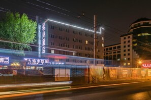 Um edifício de vários andares com sinalização iluminada, entrada coberta e uma fonte visível.
