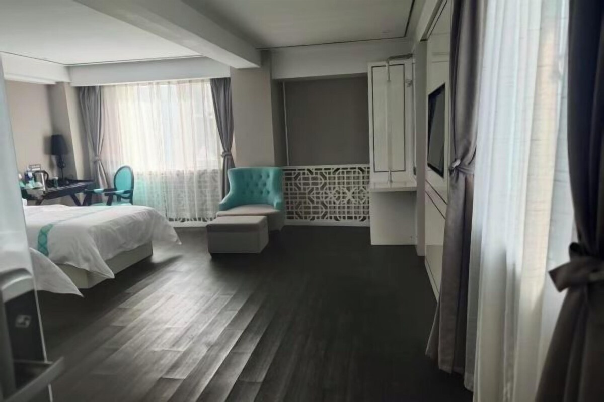 Habitación de hotel con cama, escritorio, silla, reposapiés pequeño y televisor.