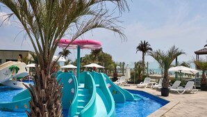 Un espace piscine doté de toboggans, de chaises longues, de parasols et de palmiers.