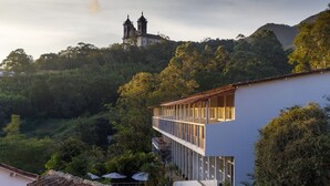 A modern building with a balcony overlooking a lush green landscape and a historic church in the background. - Grande Hotel de Ouro Preto (Ouro Preto)