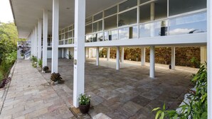 A covered outdoor area with a stone floor, white pillars, and potted plants. - Grande Hotel de Ouro Preto (Ouro Preto)