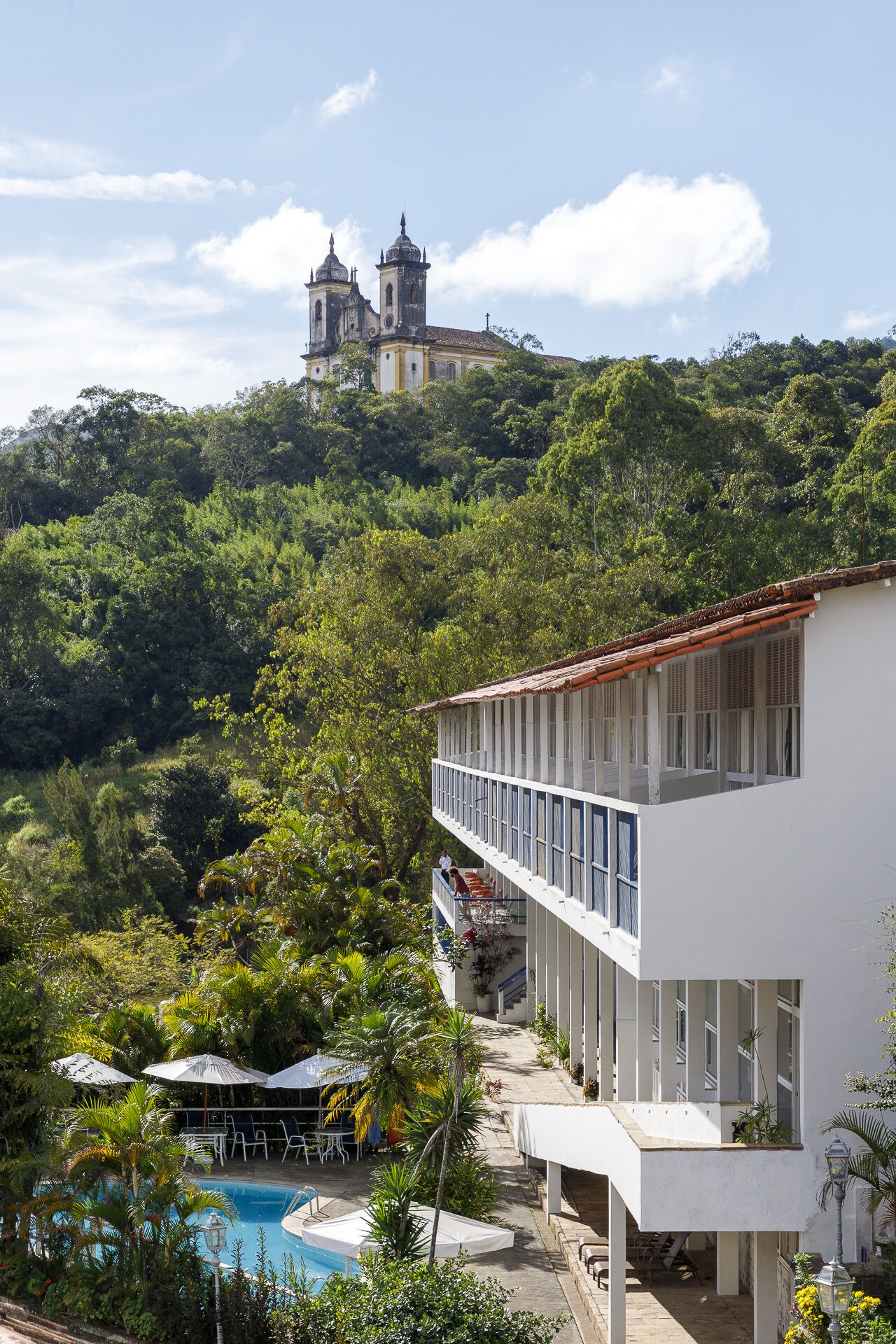 A hotel with a pool, a balcony, and a view of a church on a hill.