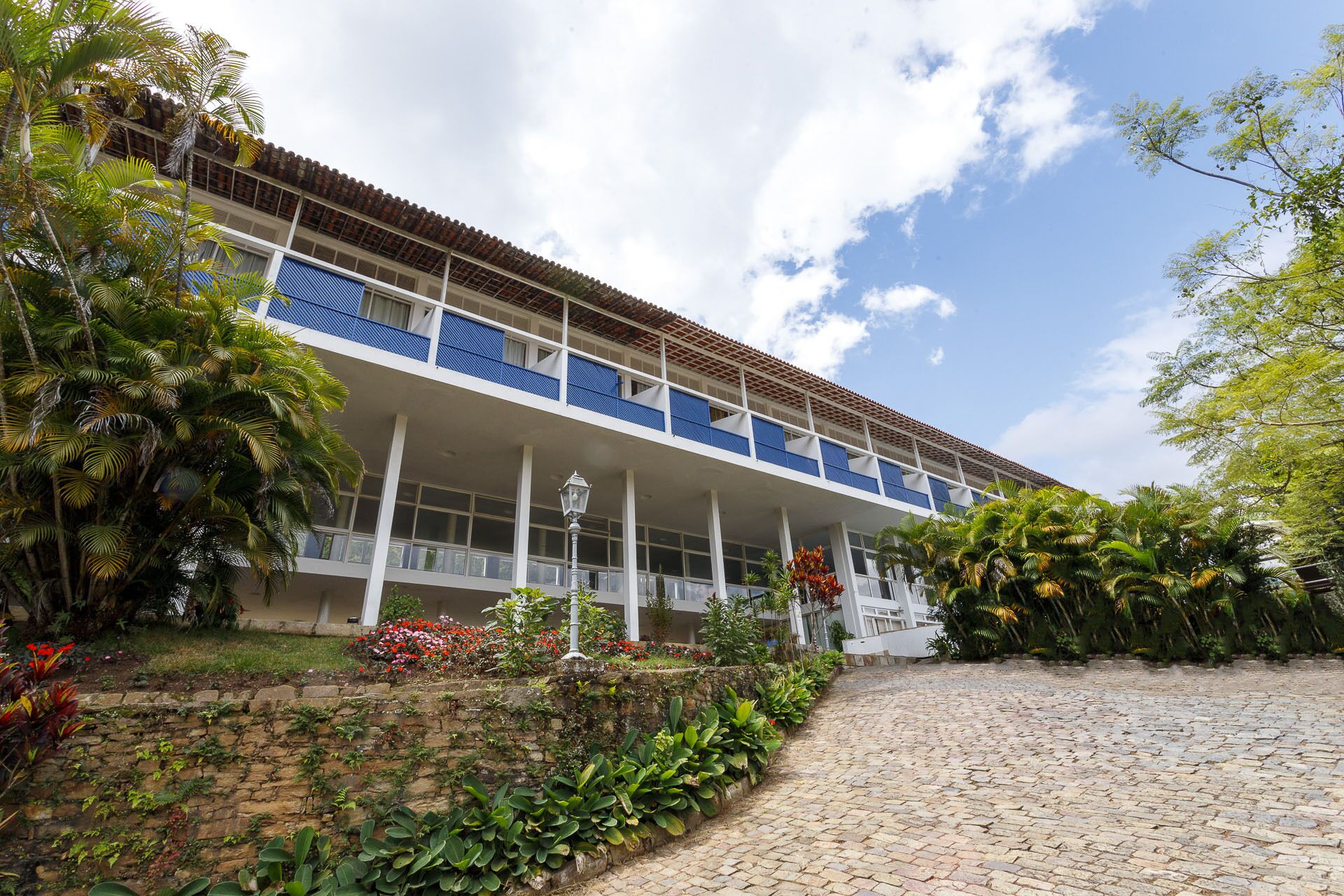 Um edifício com fachada branca, varandas azuis e um caminho de pedra que leva à entrada.