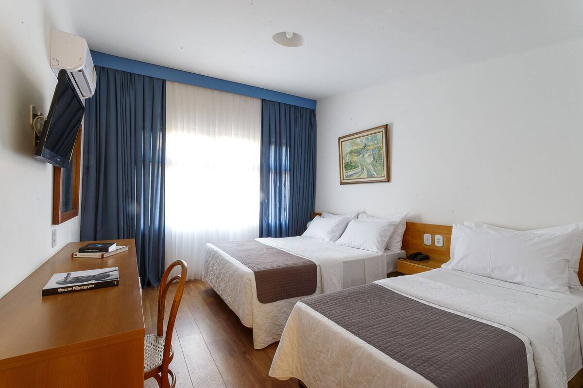 A hotel room with two beds, a desk, and a chair.
