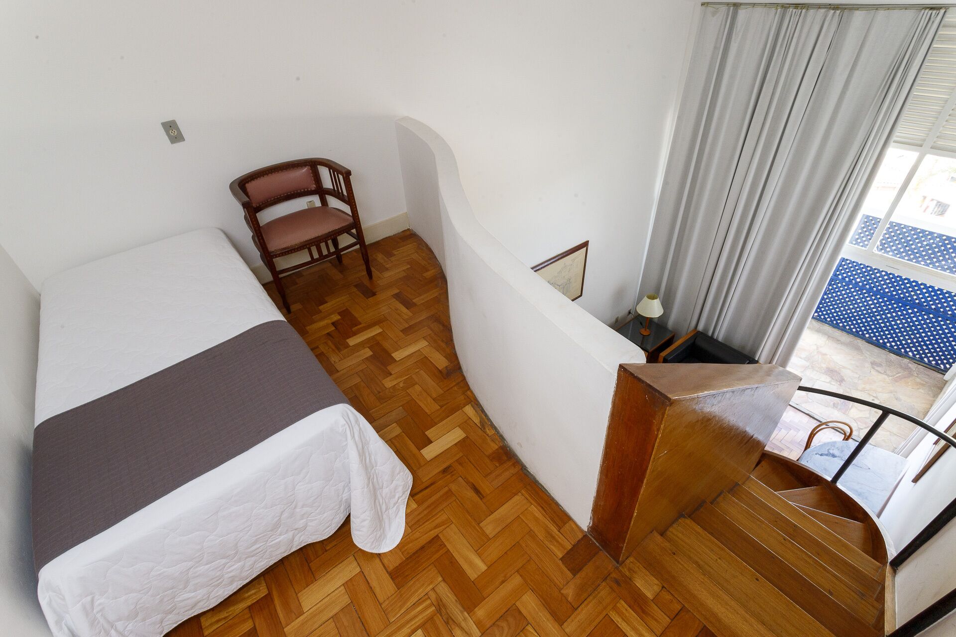 Een kamer met een bed, een stoel, een houten trap en uitzicht op buiten.
