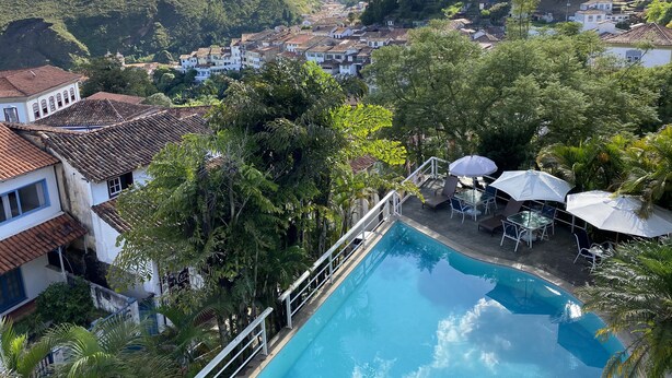 A pool area with a view of a hillside town, surrounded by lush greenery. - Grande Hotel de Ouro Preto (Ouro Preto)