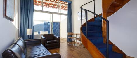 A modern living room with a wooden staircase, a sofa, and a dining area with chairs.