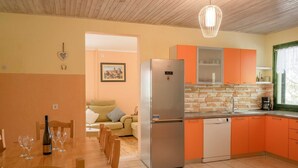 A compact kitchen with a refrigerator, orange cabinets, and a dining area with a table set for two. - Holiday Home Melanie (Blato)