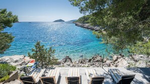A coastal view with a clear blue sea, rocky shoreline, and lounge chairs overlooking the water. - Holiday Home Melanie (Blato)