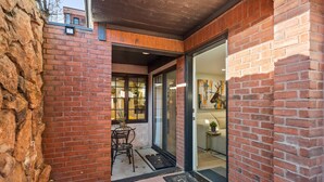 Een gevel van baksteen met een glazen deur, een klein terras en een zichtbaar interieur met een bank en decoratieve objecten.