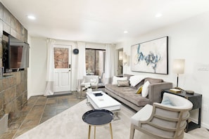 A modern living room with a stone fireplace, a large abstract painting, and a comfortable seating area with a sofa and chairs.