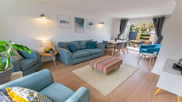 A modern living room with a sofa, a dining table, and a small kitchen area. - Oceanside | Sleeps 6 |Walk to Beach & Stylish (Croyde)