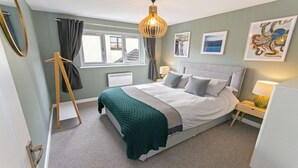 A neatly arranged bedroom with a bed, bedside tables, a hanging light fixture, a radiator, and artwork on the walls. - Oceanside | Sleeps 6 |Walk to Beach & Stylish (Croyde)