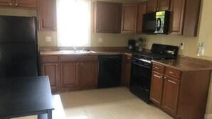 A kitchen with wooden cabinets, a black refrigerator, a microwave, a stove, and a dishwasher.