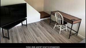 A basement with a futon, a desk, and a 55" smart TV.