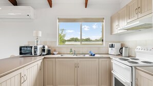 A modern kitchen with a window, built-in appliances, and light-colored cabinetry. - Settlement Sands Cowes (Cowes)