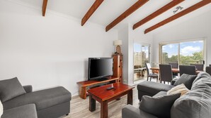A modern living room with a flat-screen TV, wooden coffee table, grey sofas, and a dining area with chairs and a table. - Settlement Sands Cowes (Cowes)