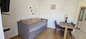 A compact living space with a sofa bed, a dining table with chairs, and a small kitchen area.