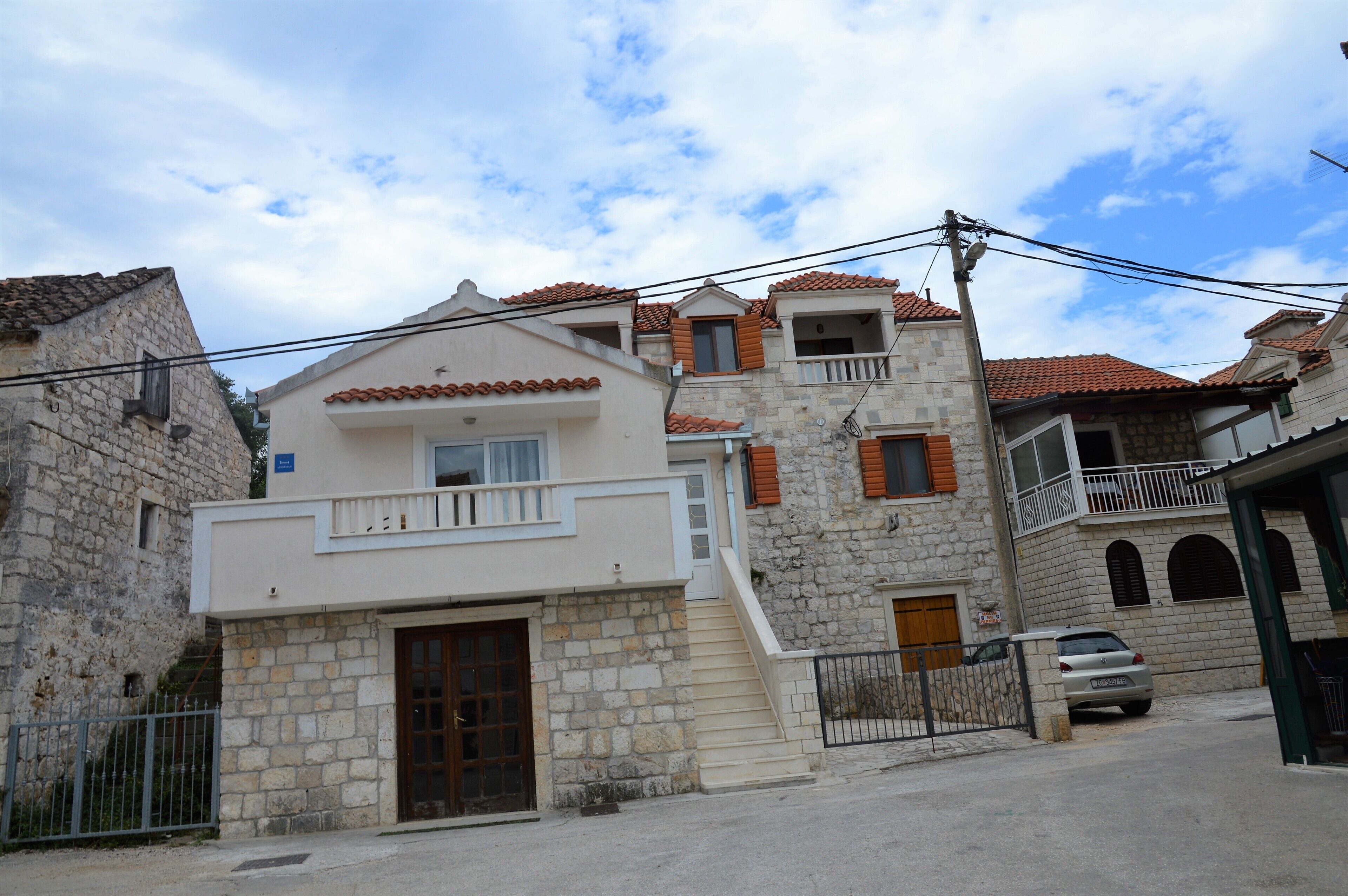 A two-story stone building with a balcony, a car parked in front, and a clear sky.