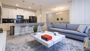 Una sala de estar moderna con un sofá gris, una mesa de centro y una cocina con armarios blancos y una encimera negra.