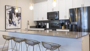 Una cocina moderna con armarios blancos, un refrigerador de acero inoxidable, un microondas e una isla central con taburetes de bar.