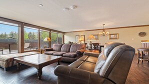Ein großzügiges Wohnzimmer mit einem großen Fenster, Ledersofas, einem Holztisch und einer Kristallleuchtre.