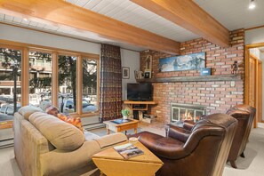 Un salon chaleureux avec une cheminée en briques, des canapés en cuir et un téléviseur posé sur un meuble en bois.