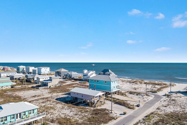 A coastal area with multiple buildings, some elevated on stilts, near a beach and ocean.